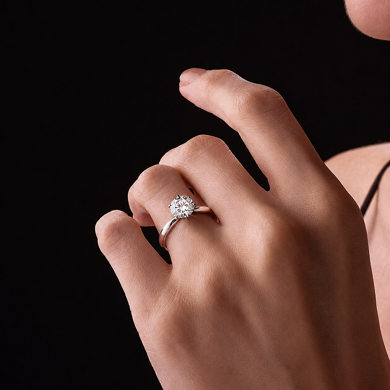 Hand wearing a 1 carat diamond ring against a black background